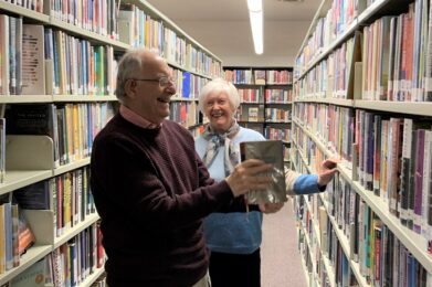 Two smiling library volunteers work to shelve books.